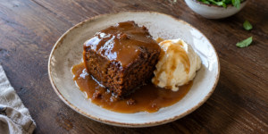 A square piece of sticky toffee pudding covered with warm toffee sauce on a plate
